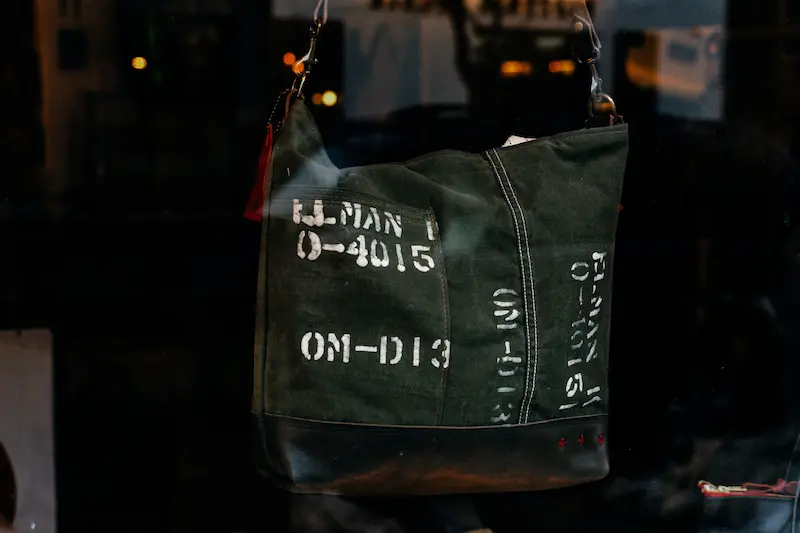 A dark olive green canvas military-style designer bag with stenciled text details, displayed in a luxury boutique window