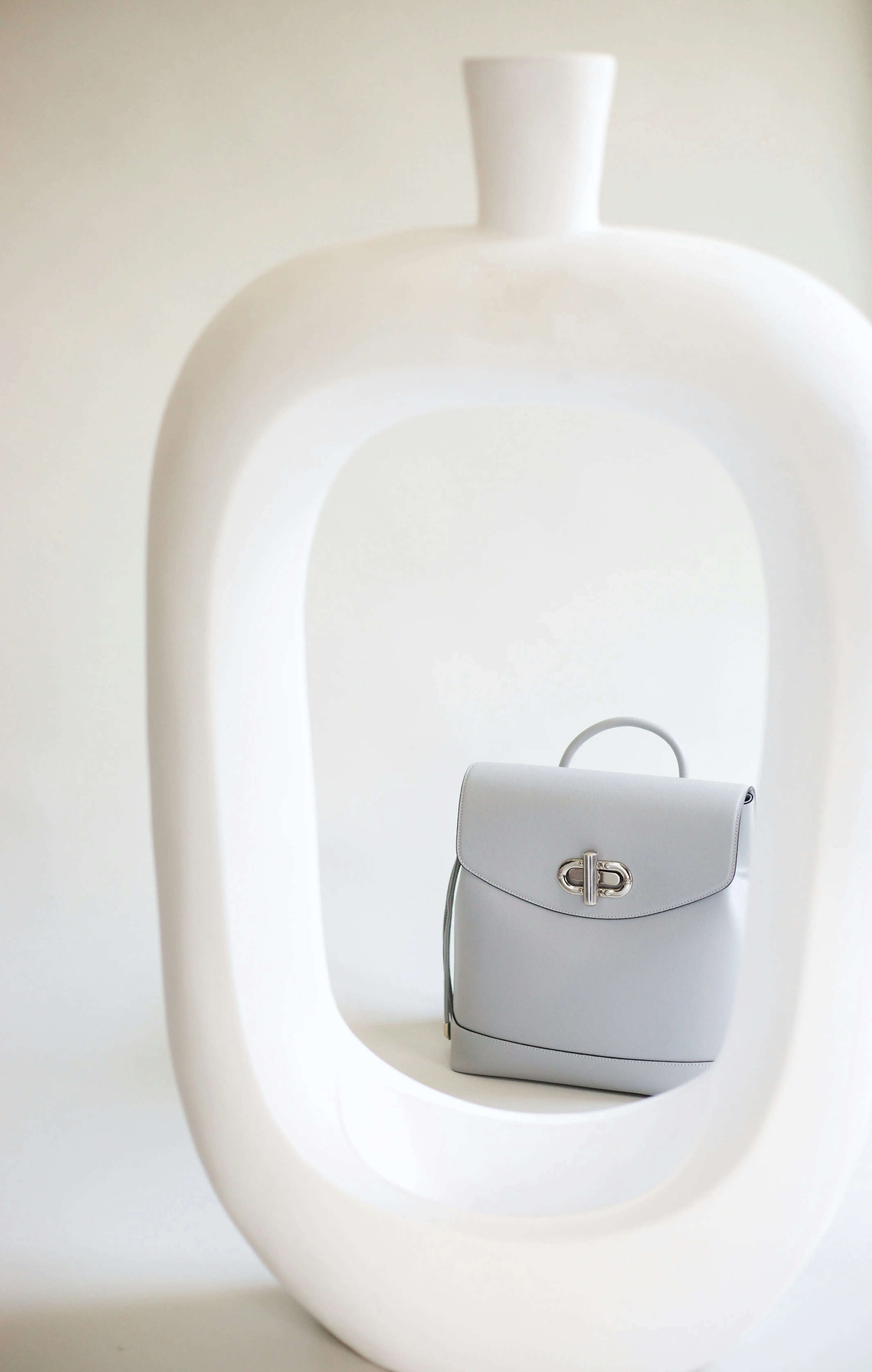 A minimalist light grey leather handbag with silver hardware displayed inside a white sculptural frame, embodying quiet luxury aesthetic