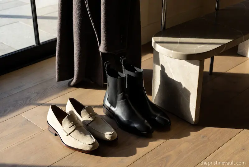 Collection of quiet luxury shoes including suede loafers and leather boots in a minimalist home setting.