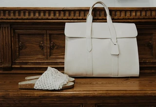 A cream leather designer tote bag and woven sandals placed on a vintage wooden dresser, illustrating proper long-term designer bag storage