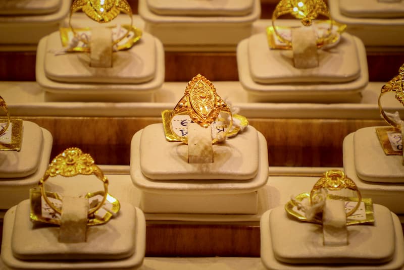Multiple ornate gold rings displayed on individual cream velvet stands in a jewelry store, representing the proper presentation and preservation of fine gold jewelry