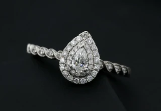 A pear-cut diamond engagement ring with double halo setting and diamond-encrusted band, displayed on a dark background showcasing fine jewelry craftsmanship