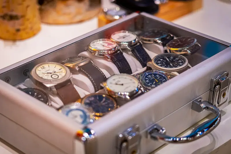 A collection of various wristwatches with different strap styles stored inside an open aluminum watch case, showcasing a practical luxury watch storage box solution