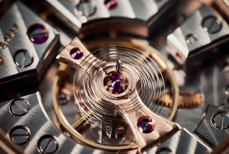 Detailed anatomy of a luxury watch movement with gold gears, balance wheel, and internal mechanical parts laid out on a watchmaker cleaning cloth for maintenance.