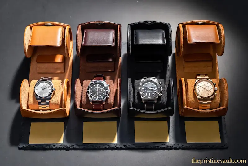 Four leather watch rolls for travel in tan, brown, black, and cognac leather each displaying a different luxury watch on suede interior with gold nameplates