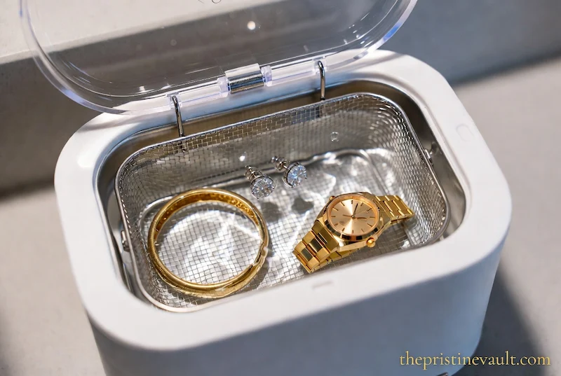 A gold watch, ring, and diamond earrings inside a white ultrasonic jewelry cleaner machine for professional maintenance