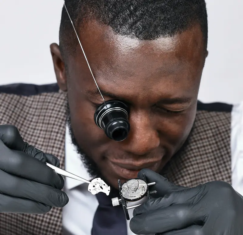 Professional watchmaker wearing loupe and black gloves carefully examining and restoring a watch
