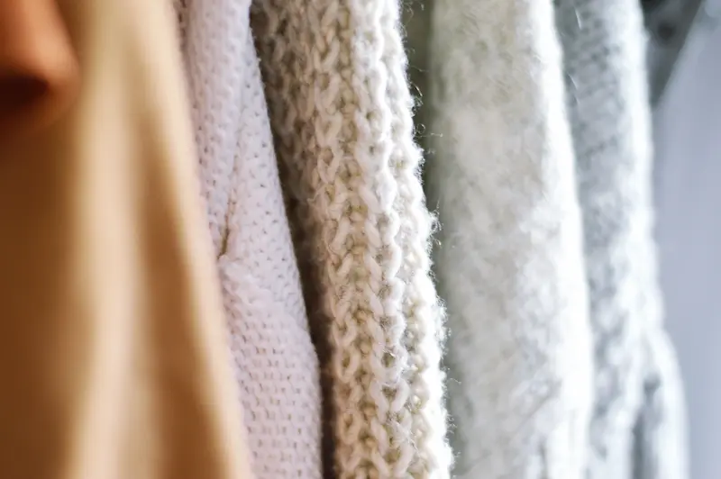 Close-up view of knit cashmere sweaters in neutral shades hanging side-by-side in a well-ventilated wardrobe