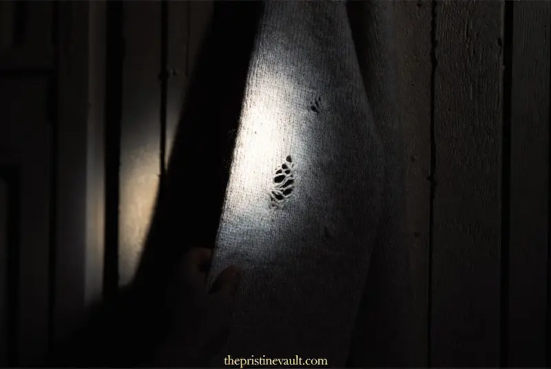 A dramatic close-up shot showing irregular holes and fiber damage on a grey wool sweater caused by moths. A spotlight highlights the moth-eaten fabric, helping owners identify early signs of infestation in their luxury cashmere collection.