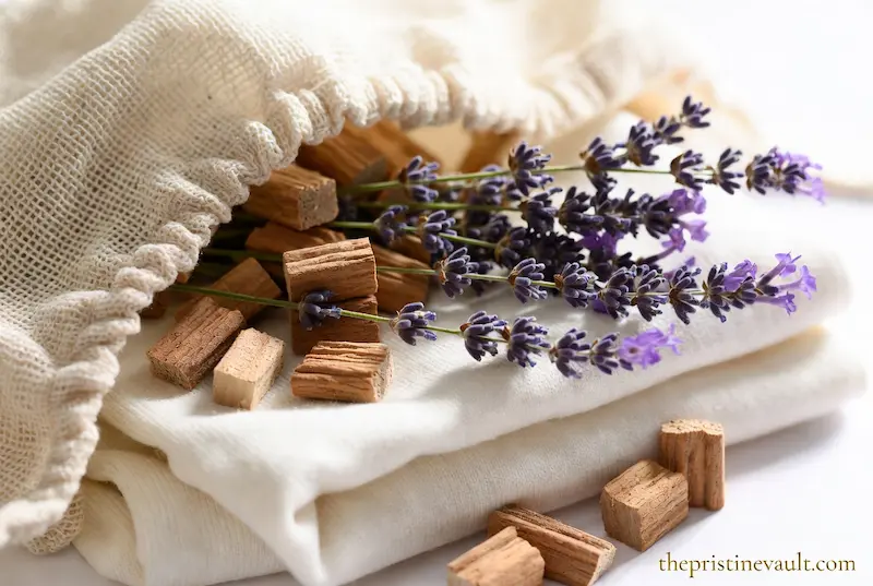A bright, macro photograph of fresh lavender sprigs and aromatic cedar wood blocks spilling out of a natural linen mesh bag. These natural moth repellents are placed on a clean, folded white sweater to provide safe, chemical-free protection for luxury cashmere and wool garments.