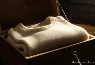 A minimalistic, high-resolution photograph of a pristine, folded cream-colored cashmere sweater stored inside a warm, polished cedar wood storage box.