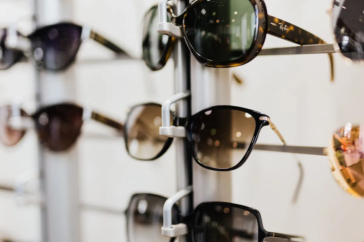 A wall-mounted optical display filled with various designer sunglasses and prescription eyeglass frames inside a LensCrafters store