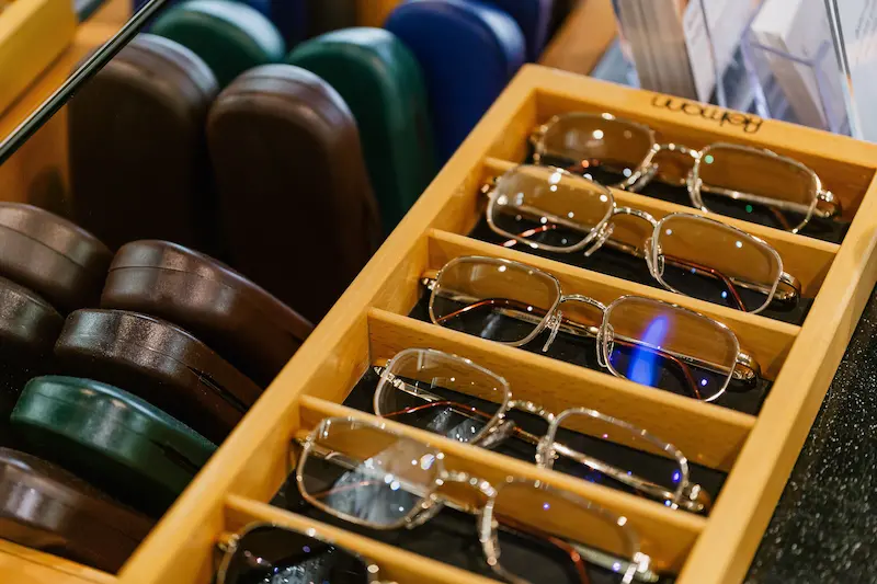 A wooden display tray neatly holding gold metal prescription eyeglass frames next to hard protective cases inside an optical shop
