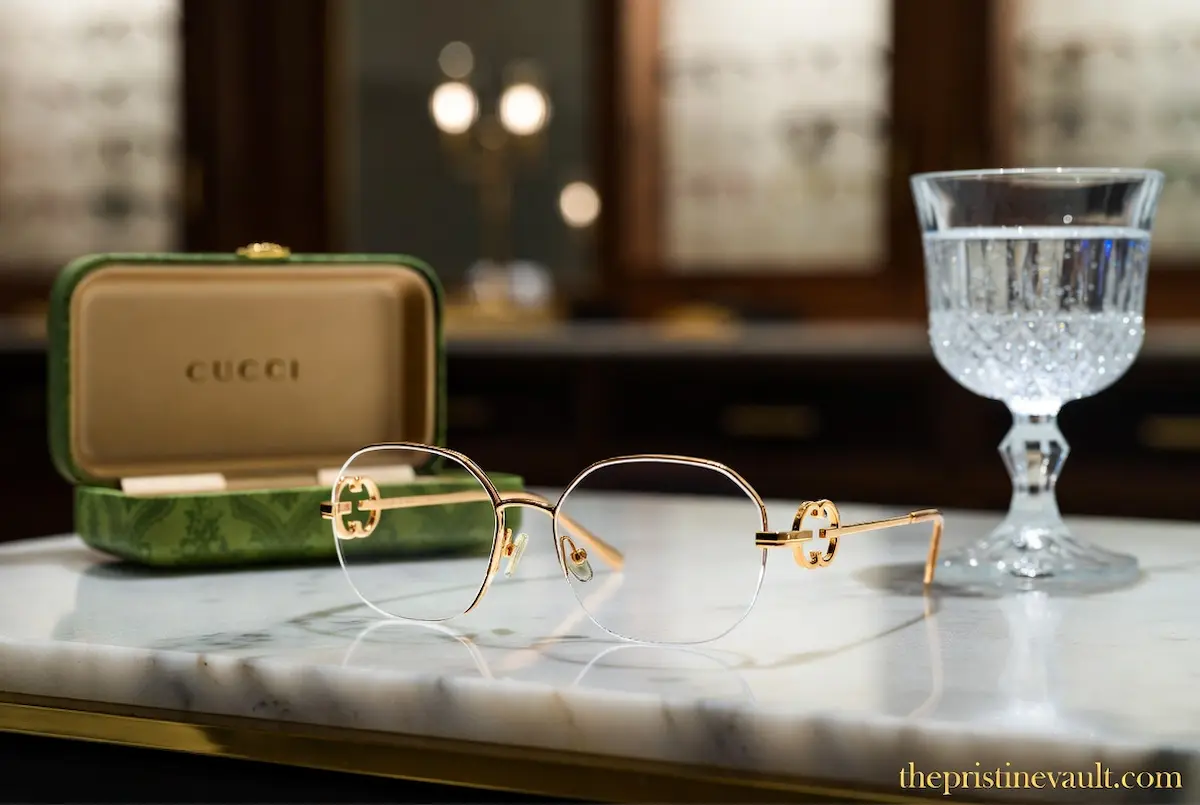 A stunning pair of official Gucci women's gold eyeglass frames and a protective green leather case resting on a white marble desk, showcasing prestigious luxury eyewear collections.