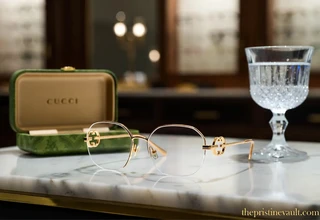 A stunning pair of official Gucci women's gold eyeglass frames and a protective green leather case resting on a white marble desk, showcasing prestigious luxury eyewear collections.