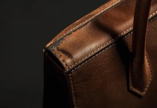 Close-up of a brown leather luxury bag showing worn-out corners, scuffed leather, and peeling edge paint near the handle