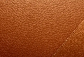 A close-up texture shot of Hermès Gold Epsom leather showing its fine embossed grain and diagonal contrast stitching