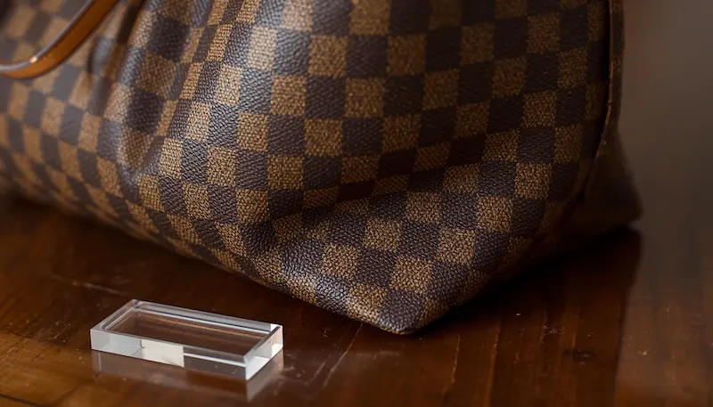Detailed view of the base sagging and canvas creasing on a Louis Vuitton Neverfull in Damier Ebene canvas, shown next to an acrylic base shaper.